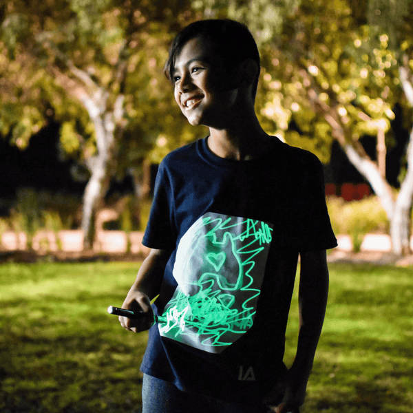 niño dibujando con linterna UV sobre camiseta negra con trazo verde brillante

