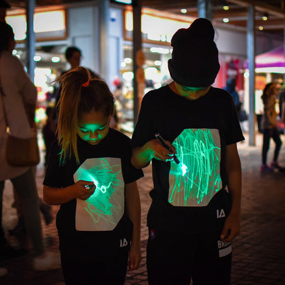 dos niños usando camisetas interactivas de brillo verde en la oscuridad

