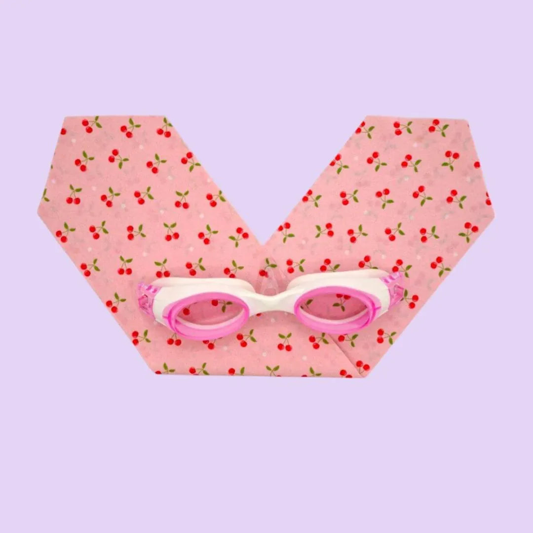 Pink and white swimming goggles on a pink fabric with cherry pattern
