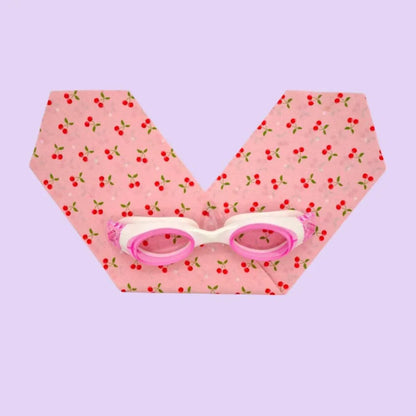 Pink and white swimming goggles on a pink fabric with cherry pattern