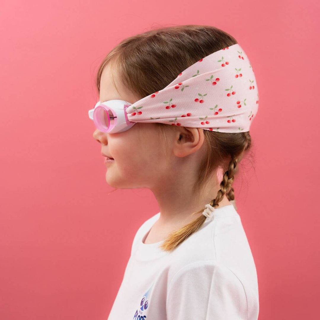 Close-up of girl wearing pink and white kids swimming goggles with cherry pattern fabric strap.
