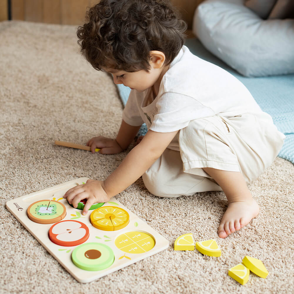 Niño sujetando piezas del Puzzle encajable de frutas con fracciones de madera de Classic World