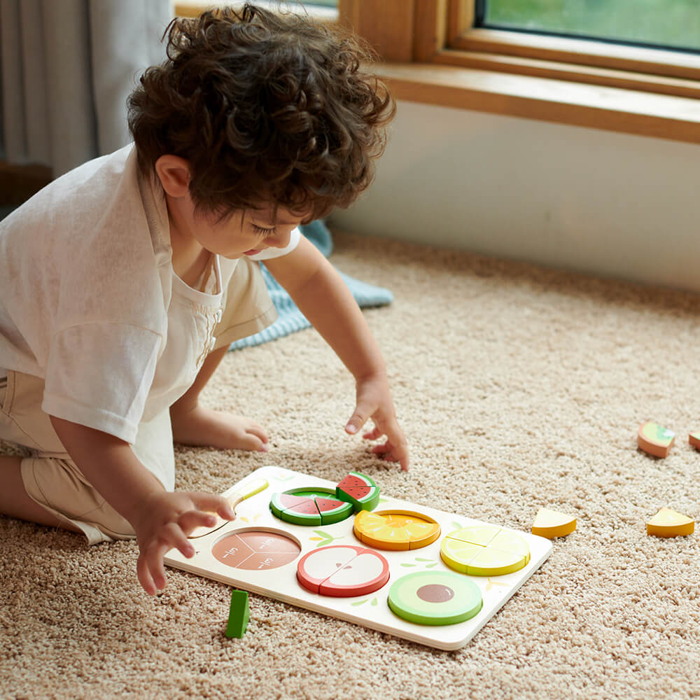 Niño colocando piezas en el Puzzle encajable de frutas con fracciones de madera de Classic World