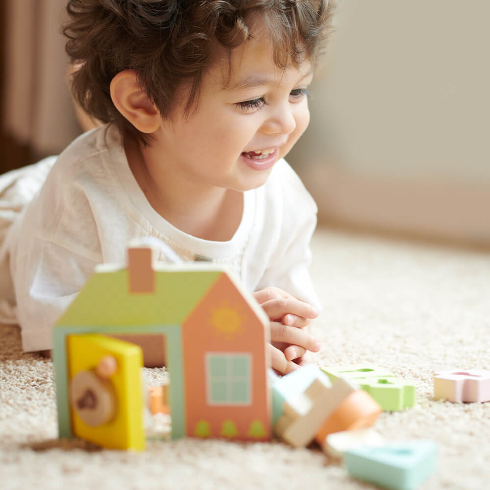 Niño riendo mientras juega con el Juego de ensartar formas con cerradura de Classic World para bebés de 18 meses
