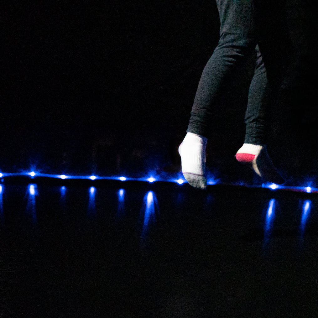 Detalle de niña saltando en cama elástica con luz LED Brightz encendida en la base por la noche