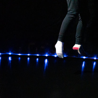 Detalle de niña saltando en cama elástica con luz LED Brightz encendida en la base por la noche