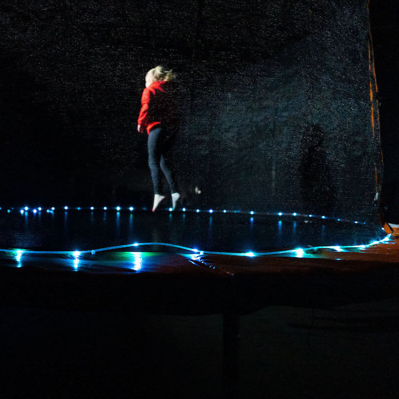 Niña saltando en cama elástica con luz LED Brightz encendida en la base por la noche