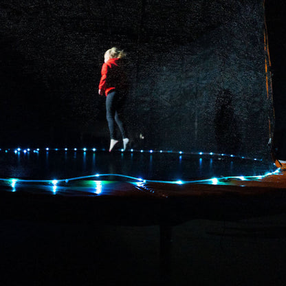 Niña saltando en cama elástica con luz LED Brightz encendida en la base por la noche