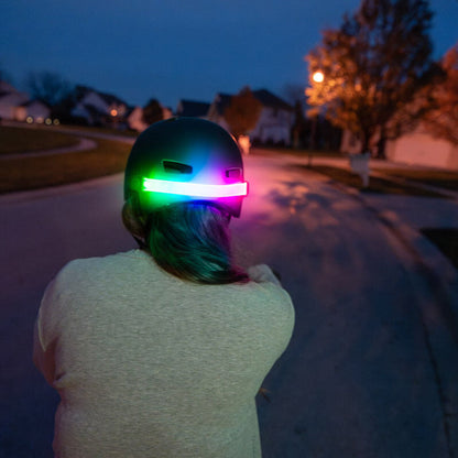 Ciclista con casco y luz multicolor Brightz encendida de noche vista desde atrás