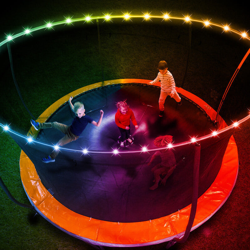 Niños saltando en cama elástica con la red iluminada por la luz LED Brightz de noche