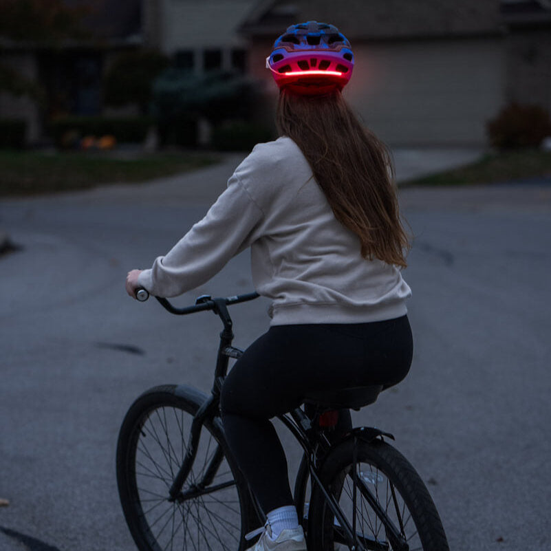 Ciclista con casco y luz roja Brightz encendida de noche vista desde atrás