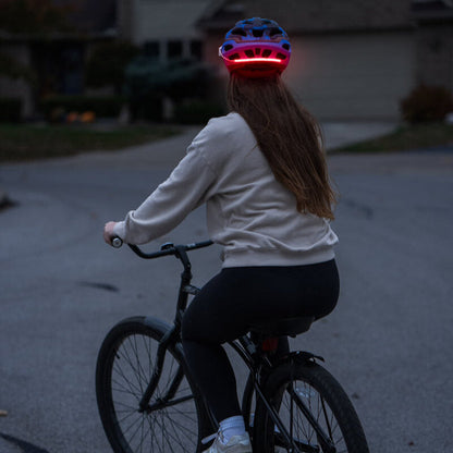 Ciclista con casco y luz roja Brightz encendida de noche vista desde atrás