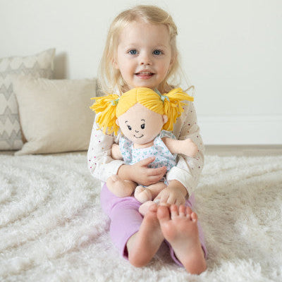 niña abranzando a la muñeca de tela Peach Love Stella con coletas rubias y vestido floral Manhattan Toy
