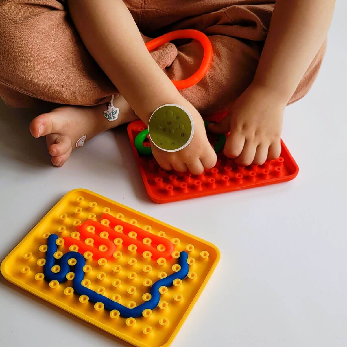 Niño sujetando y jugando con Wiggly Toy rojo, formando una figura con las tiras de silicona