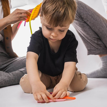 Niño desarrollando motricidad fina con Juego sensorial Wiggly Toy rojo con tiras verde y amarilla encajadas en la matriz