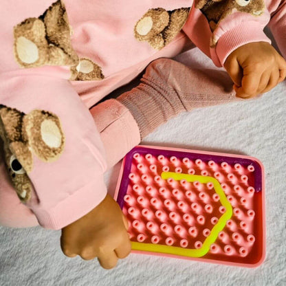 Niña jugando con juego sensorial de silicona Wiggly Toy de color rosa para desarrollar la motricidad fina